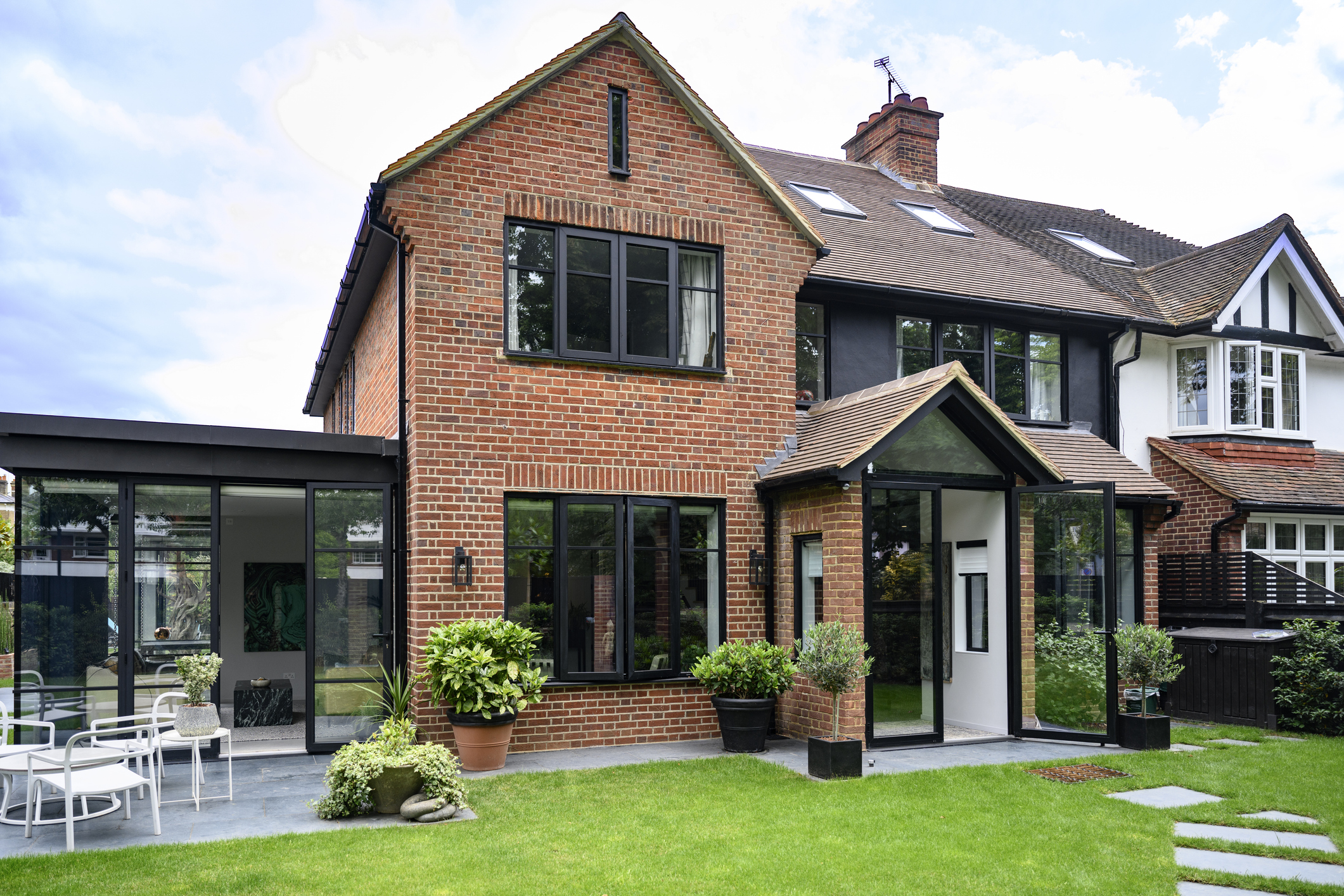 Back yard view of modern two-storey home in early summer with green grass, potted plants, patio table and chairs.