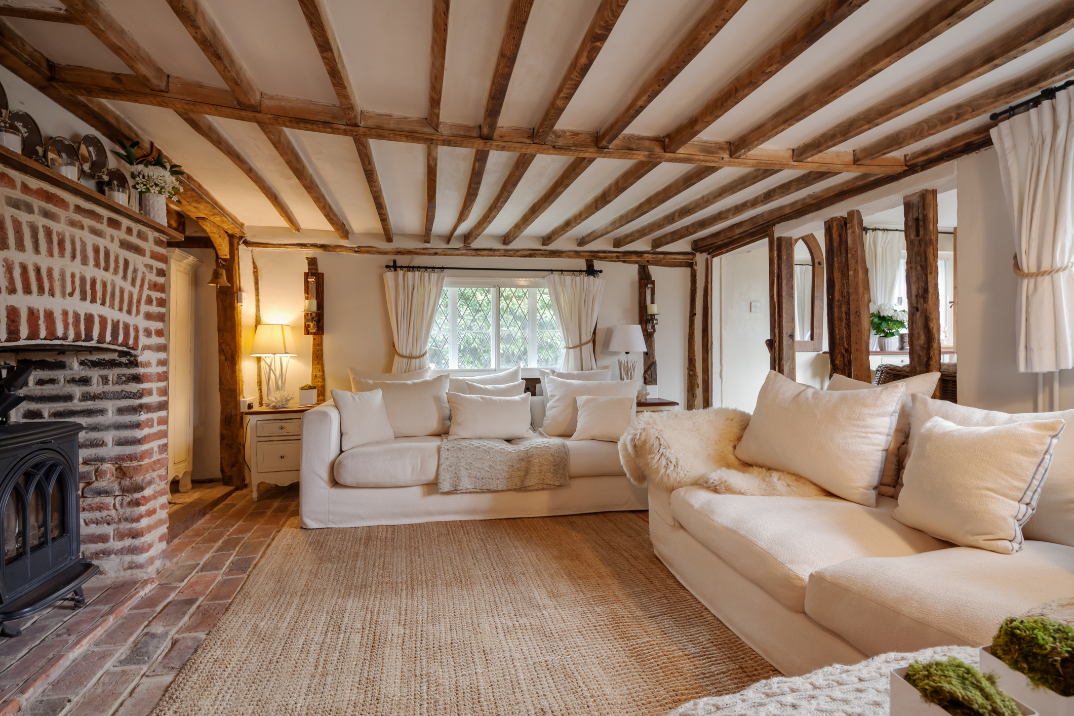 16th Century English cottage living room with cast iron fire beutifully decorated in pastel colours and furnishings with expose brick floor, expose brick chimney breast, beams and timbers, matching chairs and cushions.